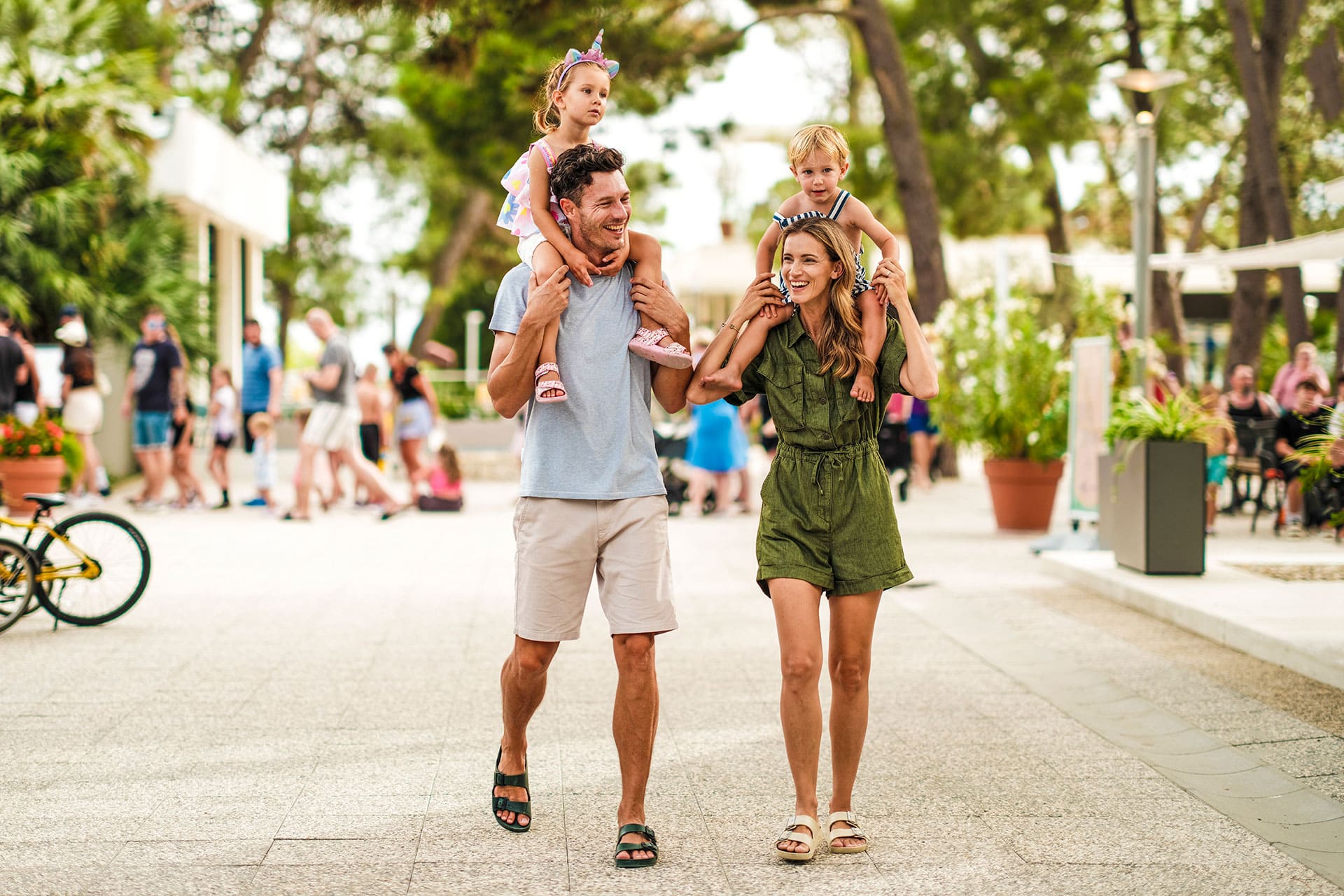 Family walking through pedestrian zone at Zaton Holiday Resort, children on parents’ shoulders Zaton Holiday Resort