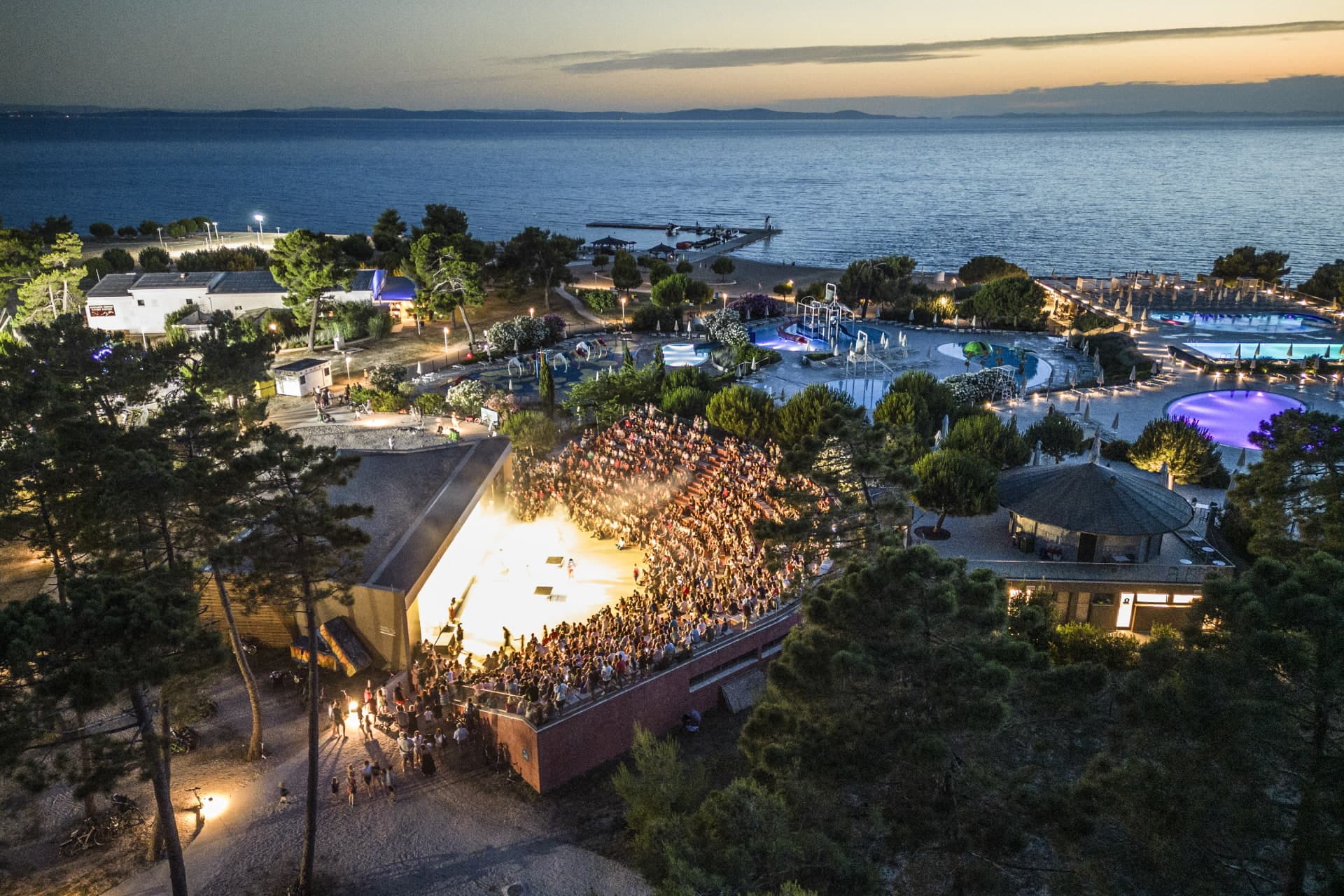 Wieczorny pokaz w amfiteatrze Zaton Holiday Resort Rodziny oglądające wieczorny spektakl w teatrze na świeżym powietrzu w Zaton Holiday Resort, położonym przy basenach