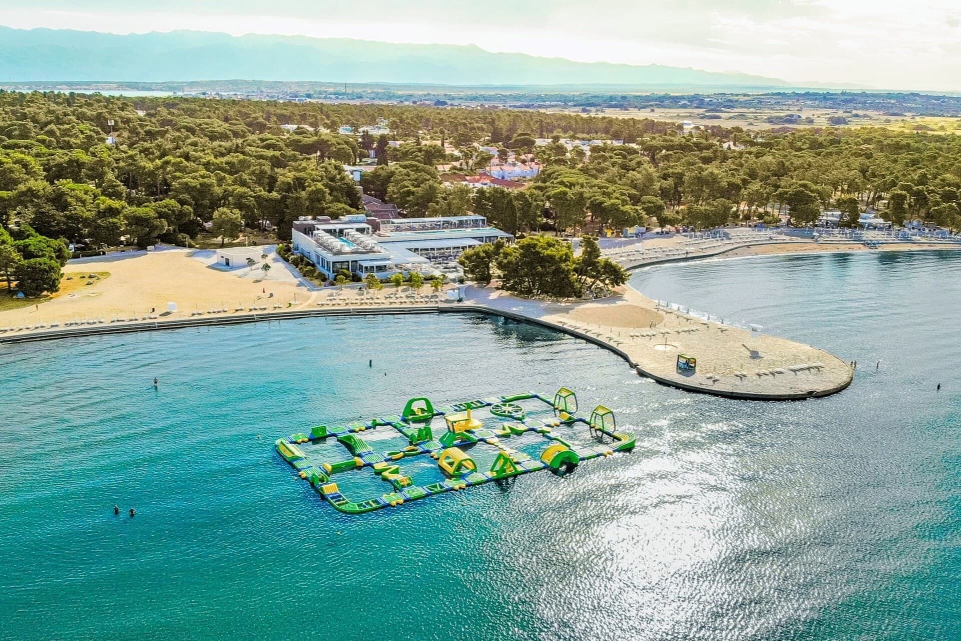 Widok z lotu ptaka na Zaton Holiday Resort w pobliżu Zadaru z piaszczystą plażą i dmuchanym parkiem wodnym, idealnym na letnie rodzinne atrakcje